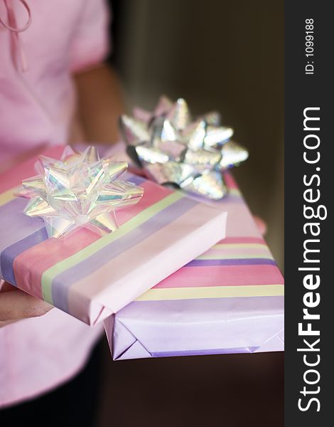 Woman dressed in pink holds pastel colored wrapped gifts that have sparkling bows on them. Woman dressed in pink holds pastel colored wrapped gifts that have sparkling bows on them.