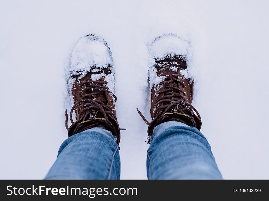 Person Wearing Brown Boots And Blue Denim Jeans Standing On Snow