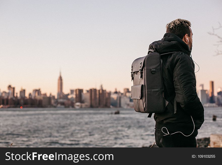 Man Wearing Black Bubble Jacket And Black Leather Backpack Near Bay