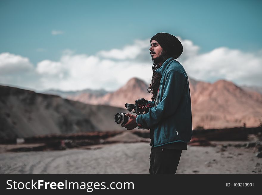Man Wearing Jacket Holding Dslr Camera on Desert