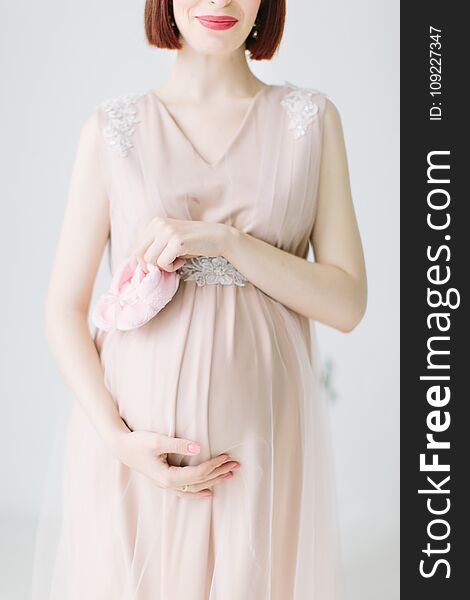 Pregnant girl is standing with pink shoes of baby