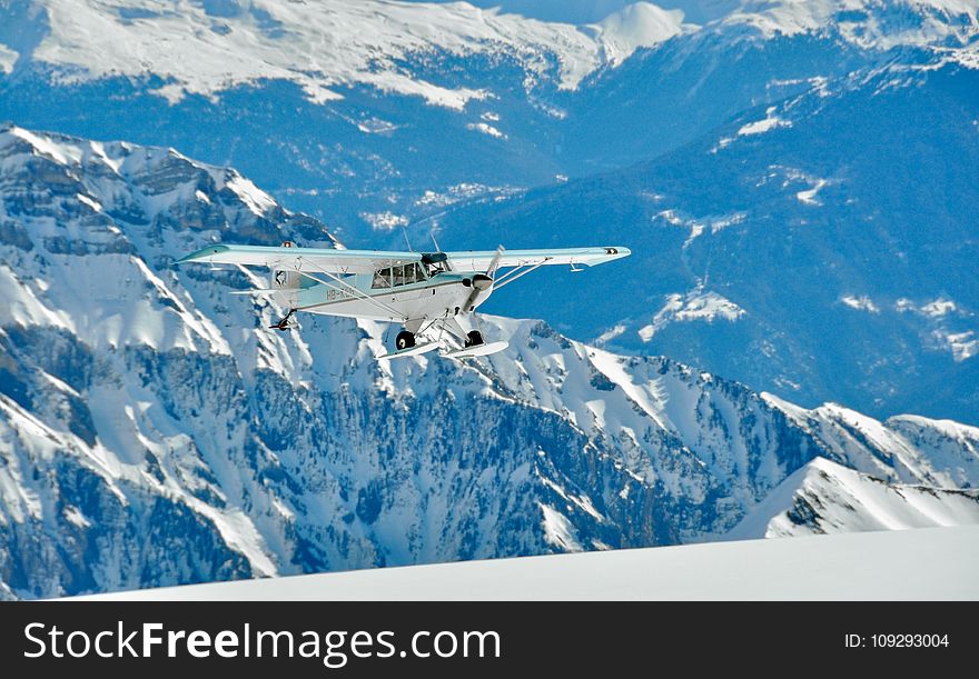 White and Green Monoplane Flying Above Mountains