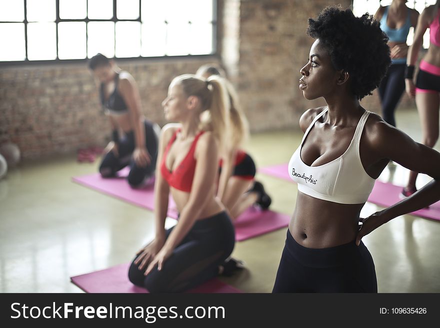 Selective Focus Photography of Woman in White Sports Brassiere Standing Near Woman Sitting on Pink Yoga Mat