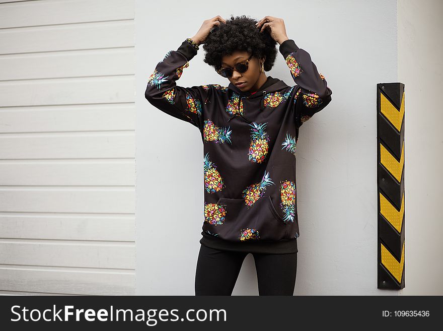 Photo of a Woman in Pineapple Print Pullover Leaning on White Wall