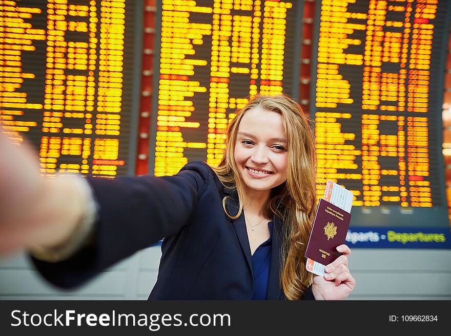 Young woman in international airport near large information display taking selfie