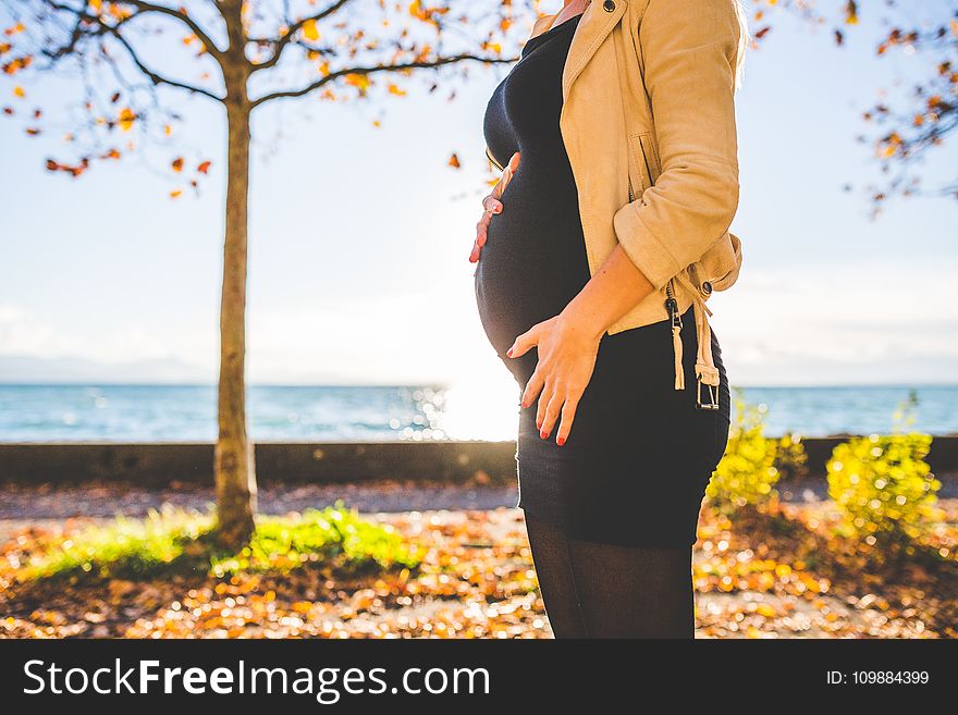 Pregnant Woman Wearing Beige Long Sleeve Shirt Standing Near Brown Tree at Daytime