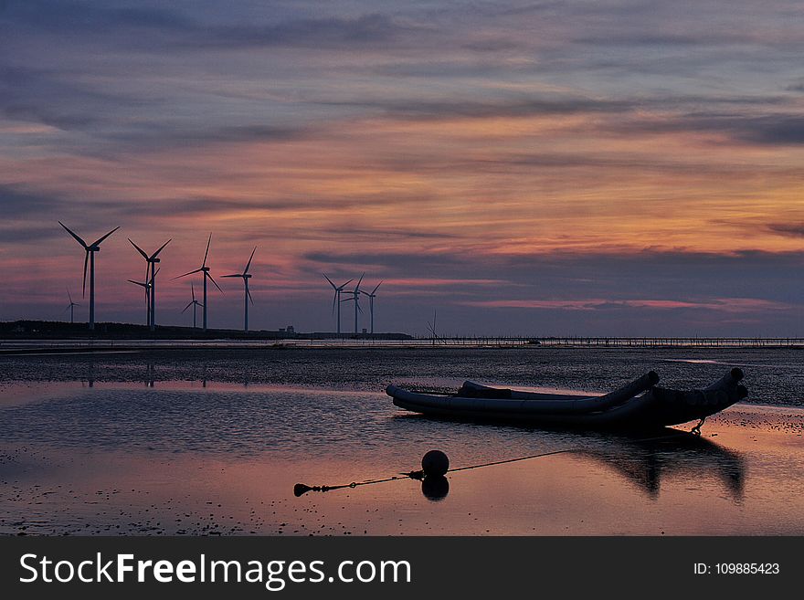 Windmills Behind Canoe Boat during Sunset