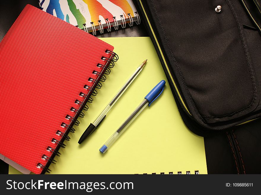 Black and Blue Pens Beside Red Covered Notebook