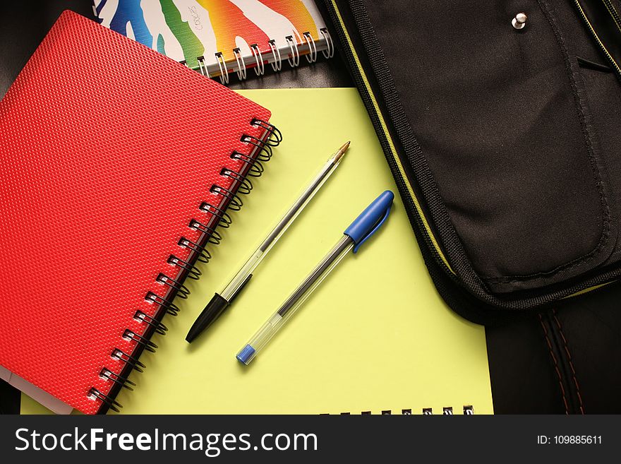 Black And Blue Pens Beside Red Covered Notebook