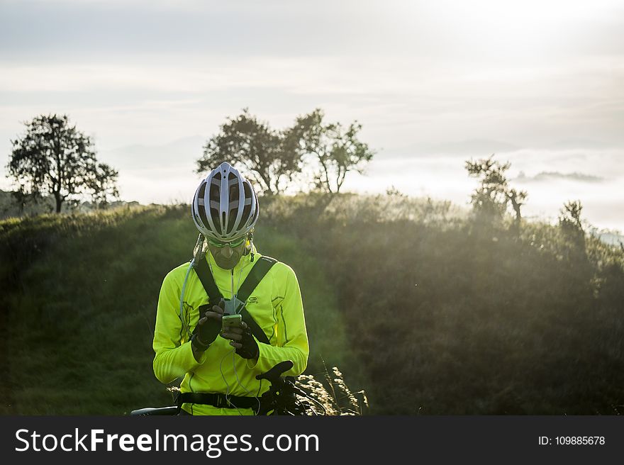 Man in Green Bicycle Suit Standing While Using His Smartphone
