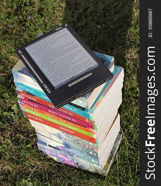 Blue Pink Gray and Green Labeled Hardbound Book Pile on Green Grass during Daytime