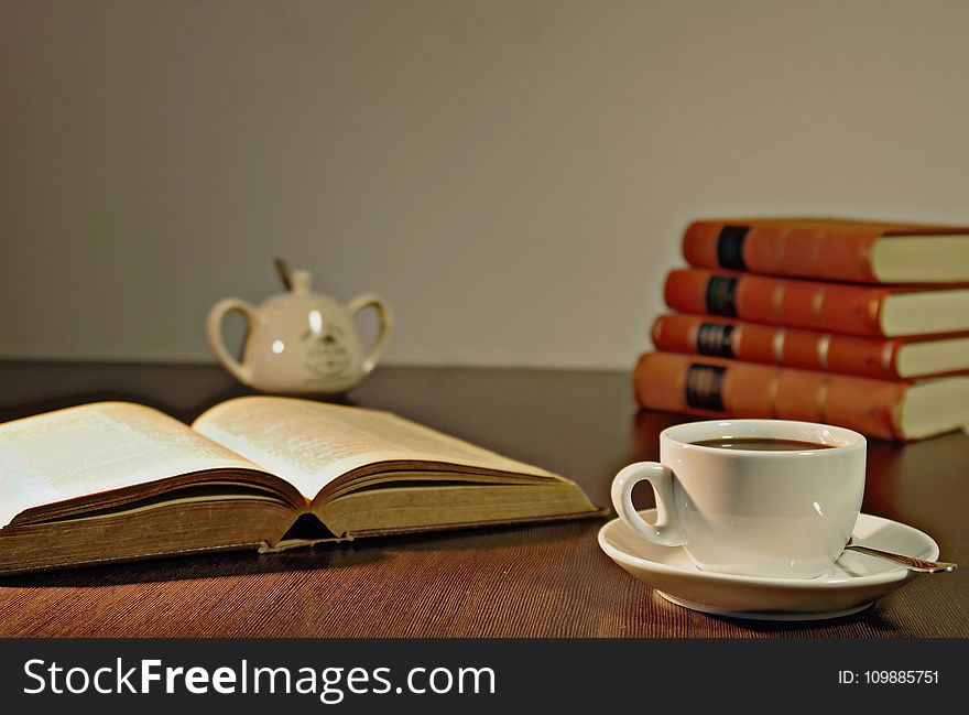 White Ceramic Teacup on Brown Wooden Table Beside Book