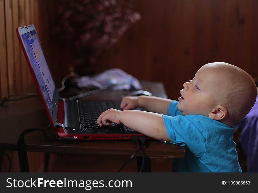 Boy Wearing Blue T Shirt Using Black Laptop Computer In A Dim Lighted Scenario