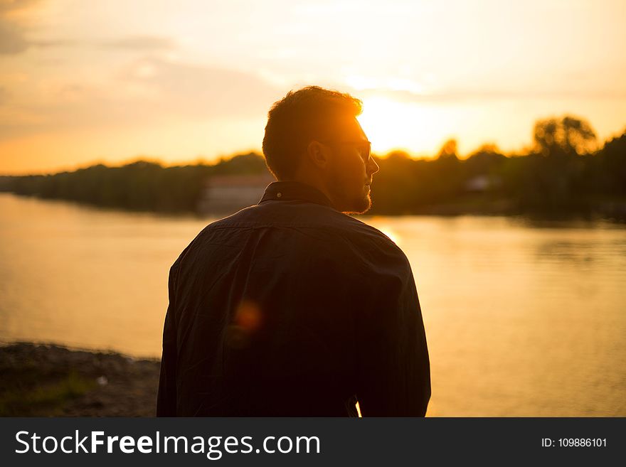 Man Sitting Near Large Body of Water Under Clear Sky during Sunset