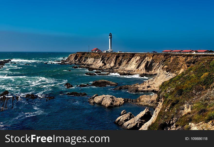 White Lighthouse Near Body Of Water Under Blue Sky During Daytime