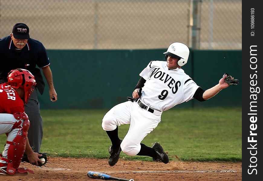 Male Baseball Player In Wolves 9 Jersey Sliding In Front Of Male In Catchers Uniform Holding Baseball On Brown Mitt