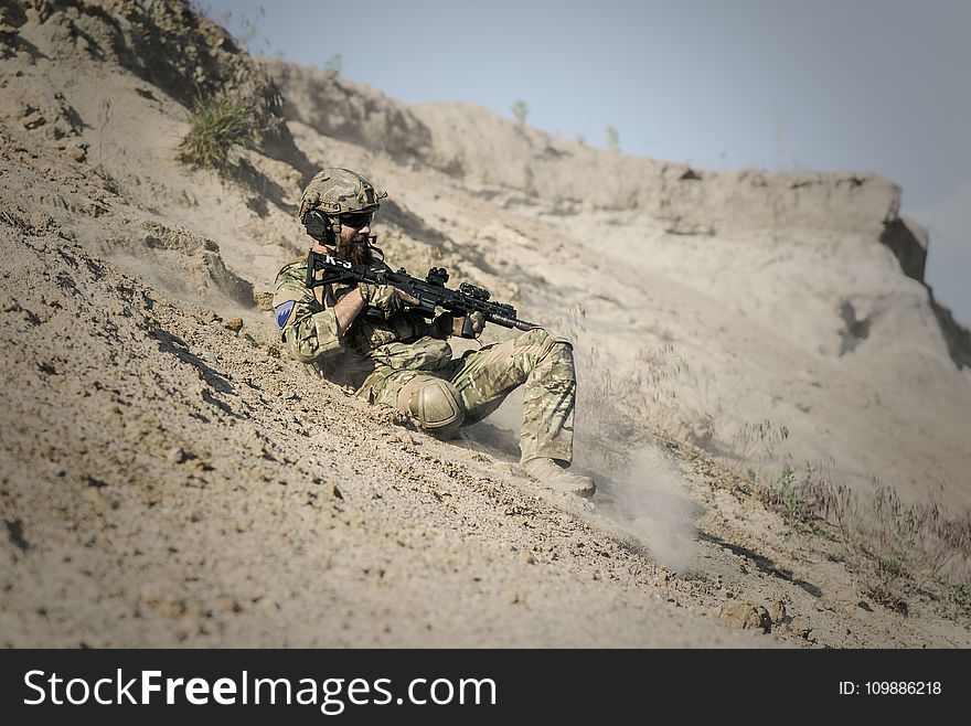 Soldier Man With Black Rifle Sliding On Cliff