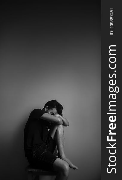 Grayscale Photography of Man Sitting Beside Wall