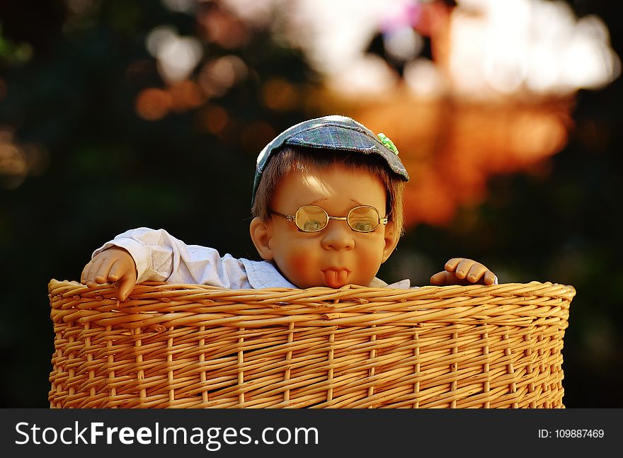 Baby Doll Wearing Eye Glasses Inside the Brown Wicker Basket