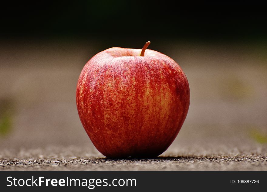 Shallow Focus Photography Of Red Apple On Gray Pavement