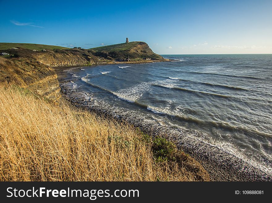 Sea Beside Mountains Under Blue Sky