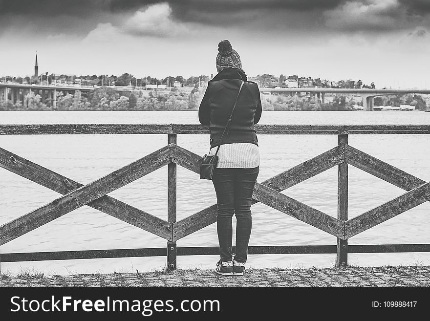 Woman Near Wooden Railing and Body of Water Grayscale Photo