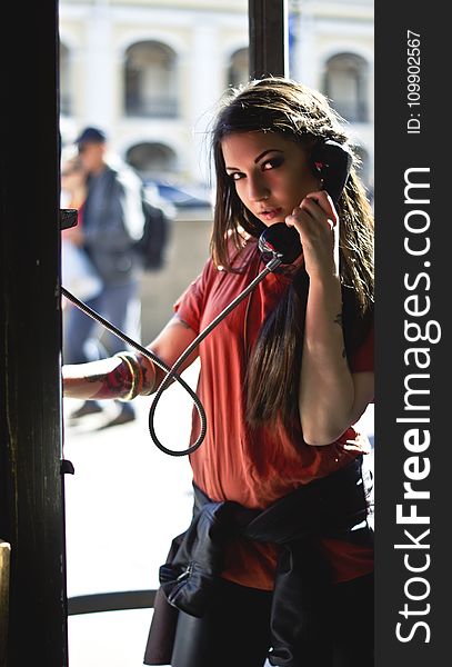 Woman in Red T-shirt Holding Telephone Inside Telephone Booth