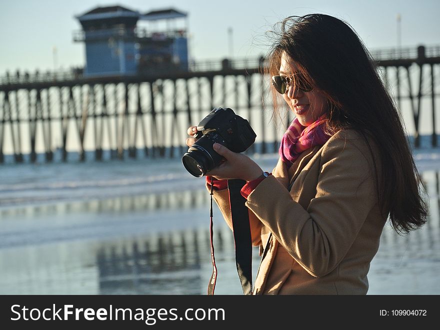 Selective Focus Photography Of Woman Holding Her Camera Near Seashore