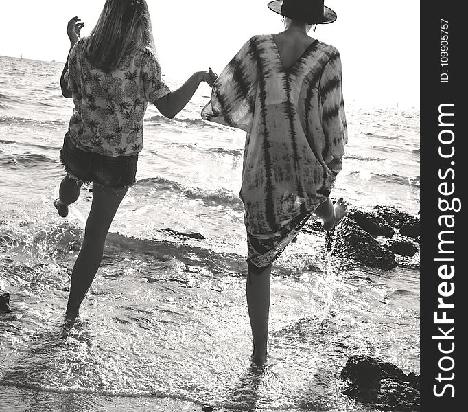 Grayscale Photograph Of 2 Women Holding Hands While Walking On Sea Shore