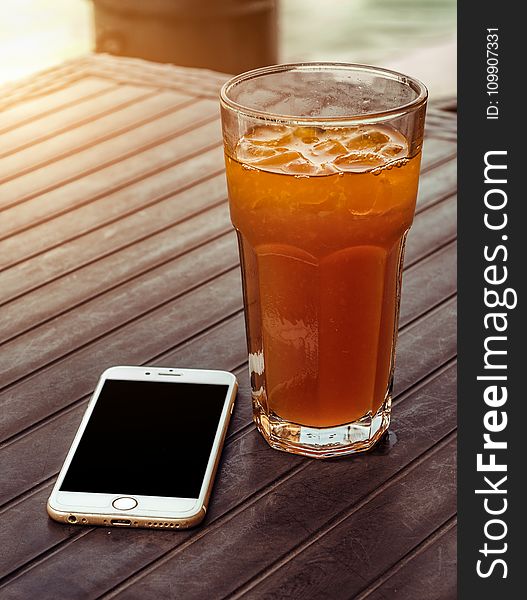 Orange Juice in Clear Drinking Glass Besides Gold Iphone 6 on Brown Wooden Table
