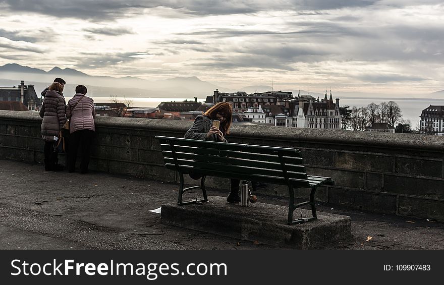 Woman Taking Photo While Sitting on the Bench Behind the Building Scenery