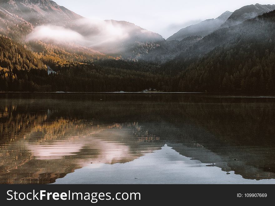 Mountain Reflection on Body of Water Under White Sky at