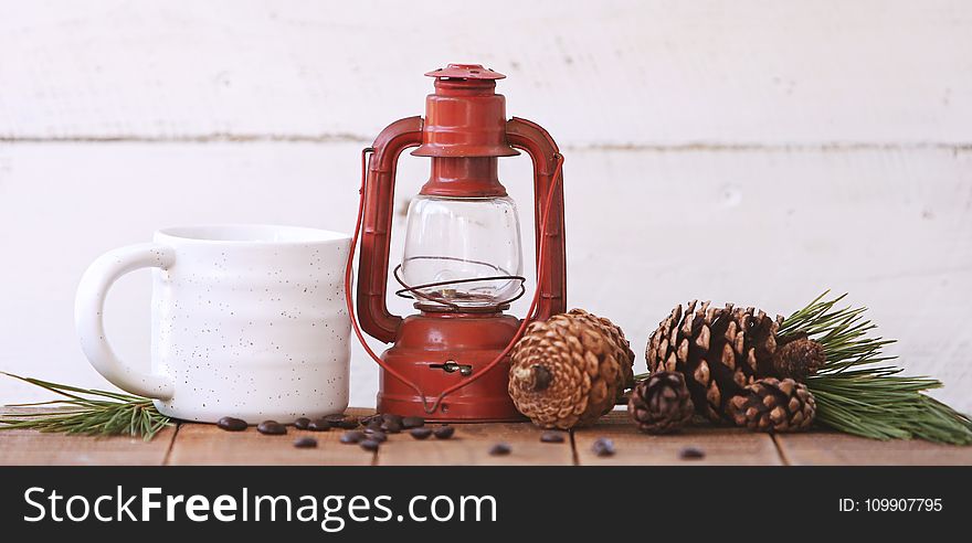 Red Kerosene Lantern Beside White Ceramic Mug on Brown Wooden Table