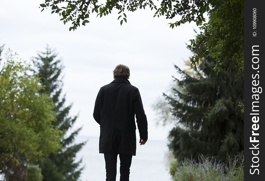 Shallow Focus Photography Of Man Wearing Black Coat And Black Pants Standing Beside Green Trees