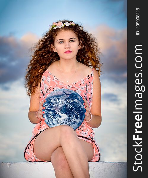 Woman Wearing Pink Floral Sleeveless Romper Sitting on Gray Concrete Holding Earth Globe