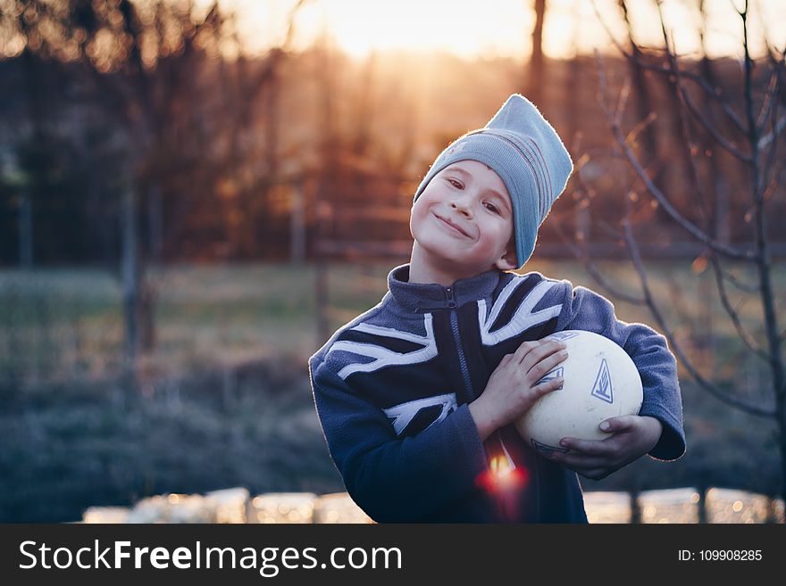 Selective Focus Photography of Boy Wearing Blue United Kingdom Print Zip-up Jacket Carrying White Ball