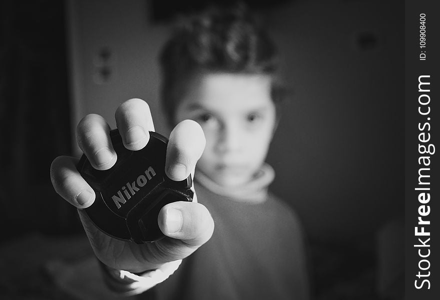 Selective Focus Photography of Boy Holding Nikon Lens Cover