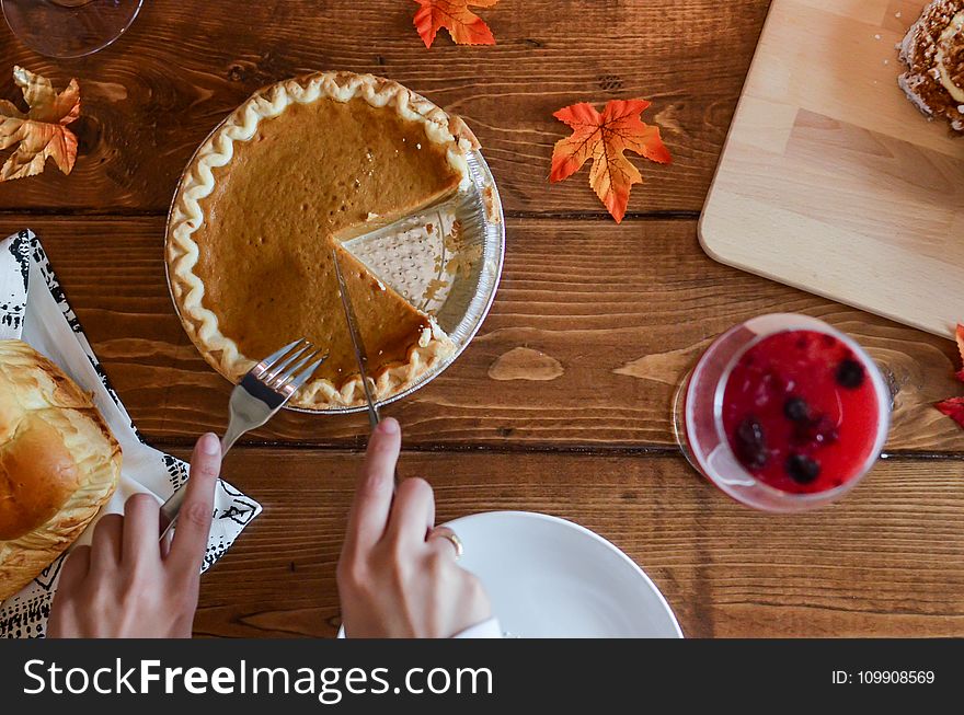 Person Holding Knife and Fork Cutting Slice of Pie on Brown Wooden Table