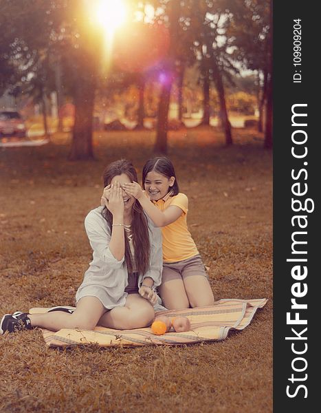 Two Women Sitting on Brown Picnic Mat during Sunset