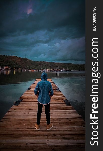 Man Wearing Blue Hoodie Standing On Wooden Dock