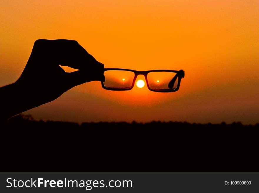 Silhouette Of Person&x27;s Hand Holding Eyeglasses During Golden Hour
