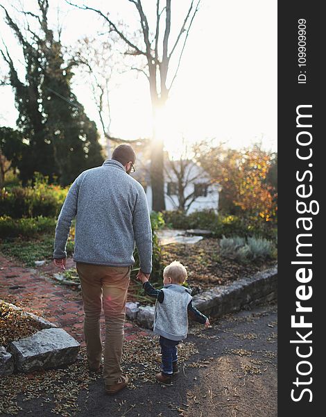 Man Holding Hands With Baby While Walking Through Pathway Facing Sunlight