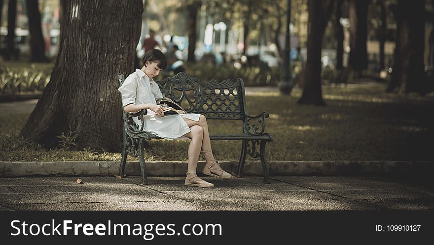 Woman Sitting on Metal Bench on Park While Reading Book