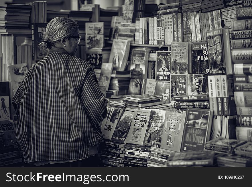 Person Standing in Front of Assorted Books in Gray Scale Photography