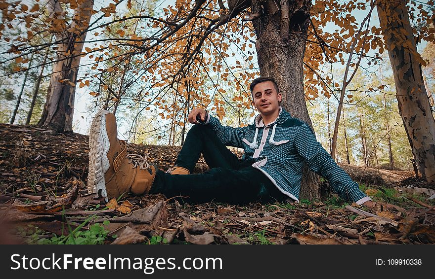 Man Wearing Green Jacket Sitting on Ground Near Tree