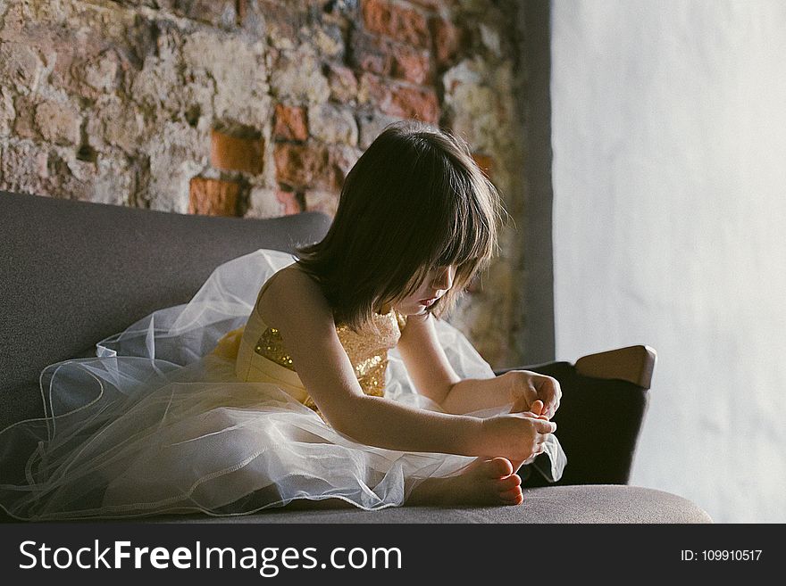 Girl in Yellow-and-white Dress Sitting on Couch While Holding Her Foot