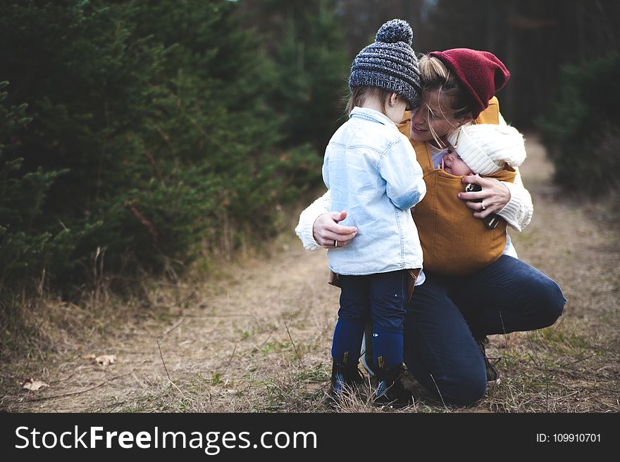 Woman With Brown Baby Carrier And Little Kid In White Jacket