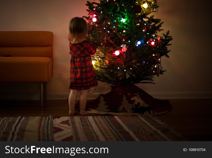 Girl in Red and Black Dress Standing in Front of Christmas Tree Inside Room