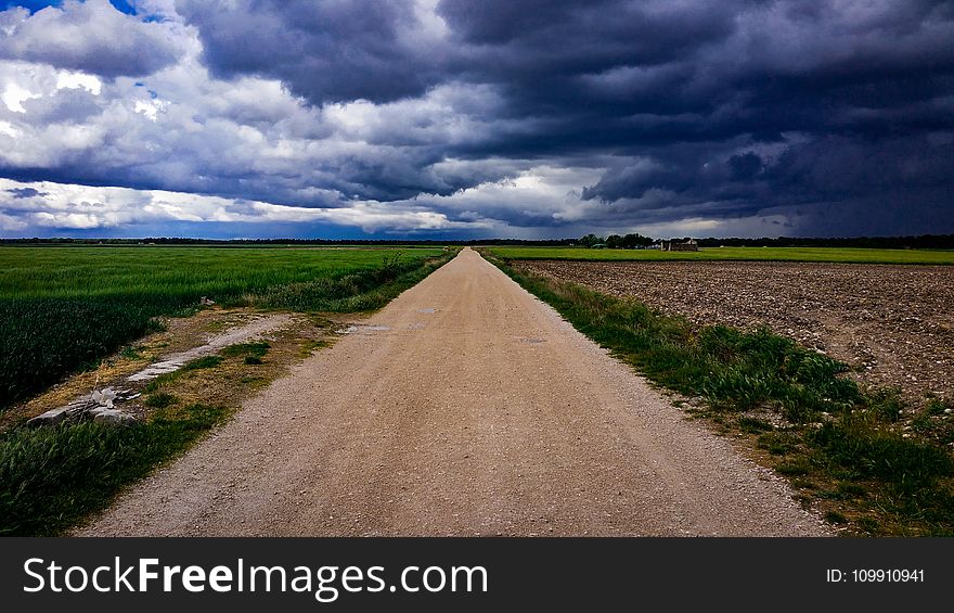 Dirt Road Surrounded With Green Field Under Cloudy Sky