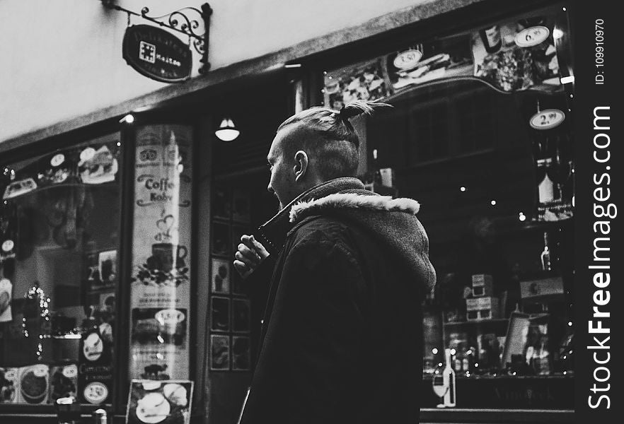 Grayscale Photograph of Man Walking Past by Shop